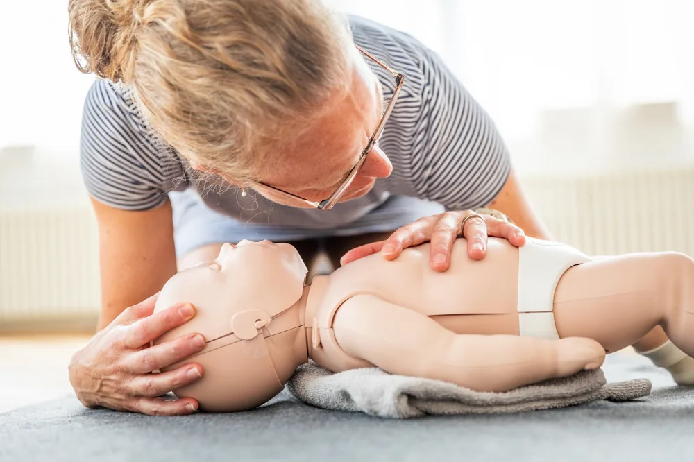 Une participante penchée sur un mannequin nourrisson, les deux mains sur son thorax, s'exerce au massage cardiaque