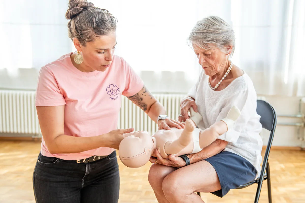 Emilie Grand guide une grand-mère qui tient un mannequin nourrisson sur ses genoux