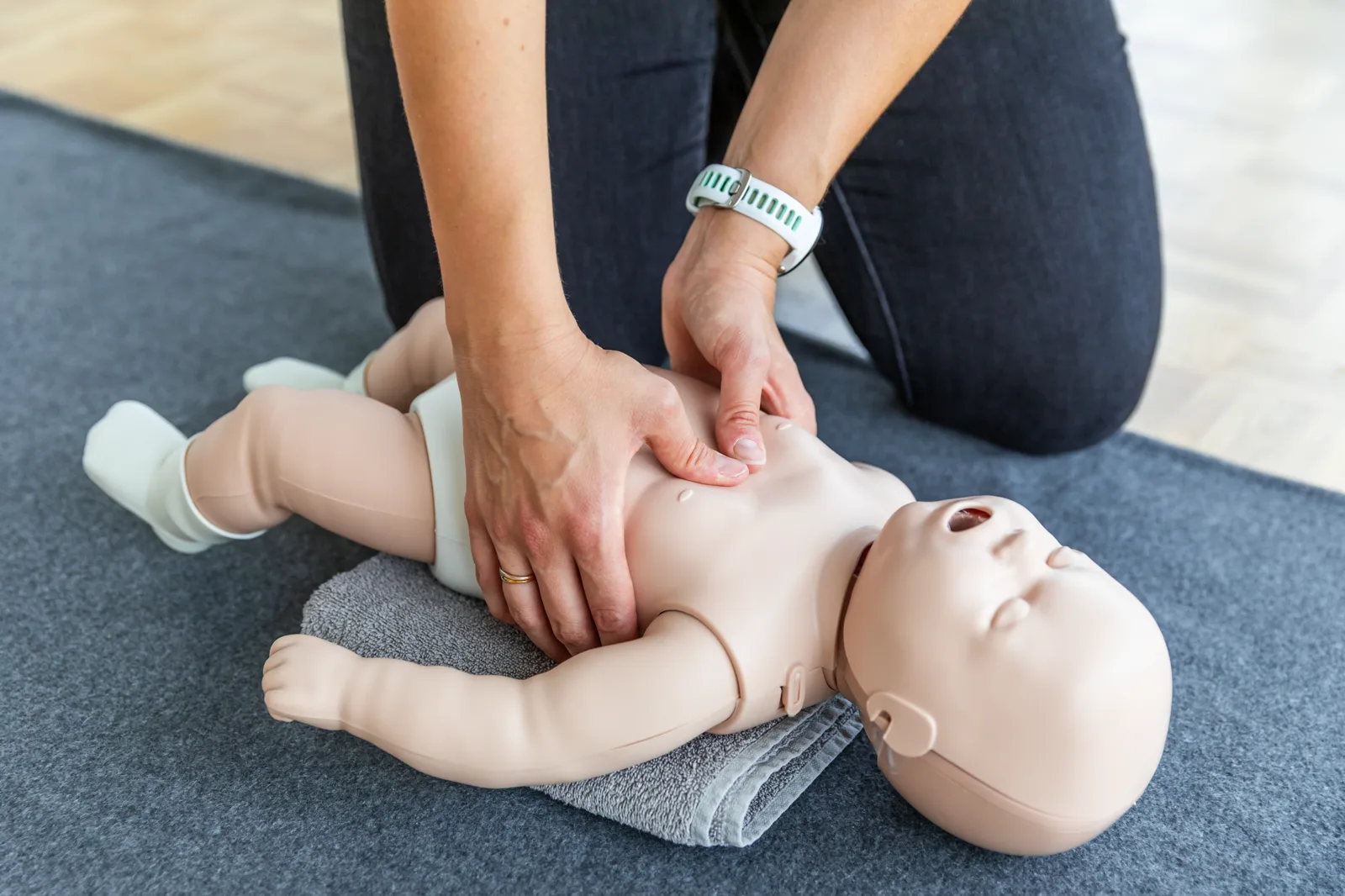Les deux mains d'une participante sur le thorax d'un mannequin nourrisson, en plein massage cardiaque