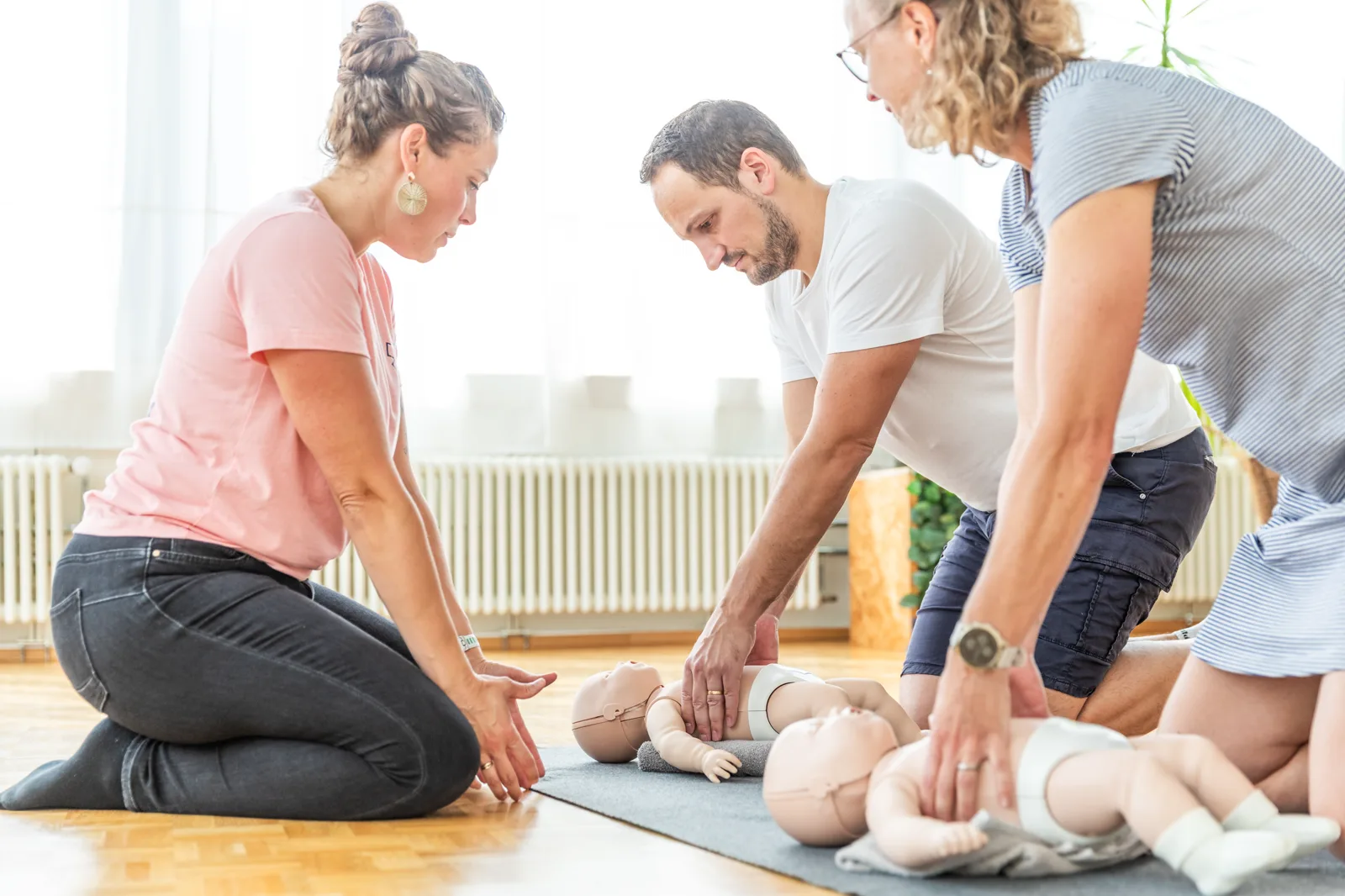 Trois participants s'exercent au massage cardiaque sur des mannequins nourrisson, au sol
